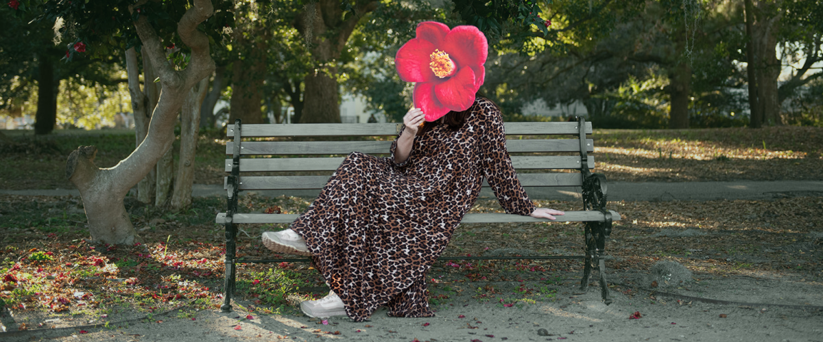 Woman sitting on a bench holding a red flower cutout covering her face