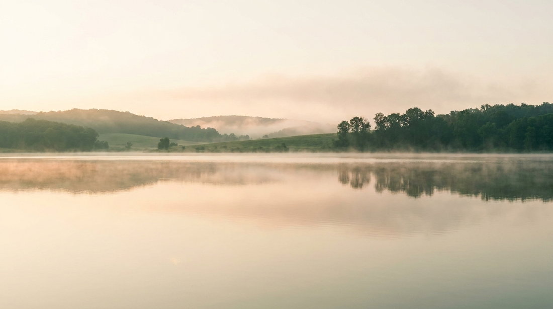 Still calm water at soft dawn with gentle mist, serene horizon