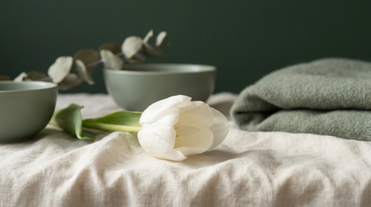 A single white tulip resting on cream linen in soft light, quiet dignified mood.