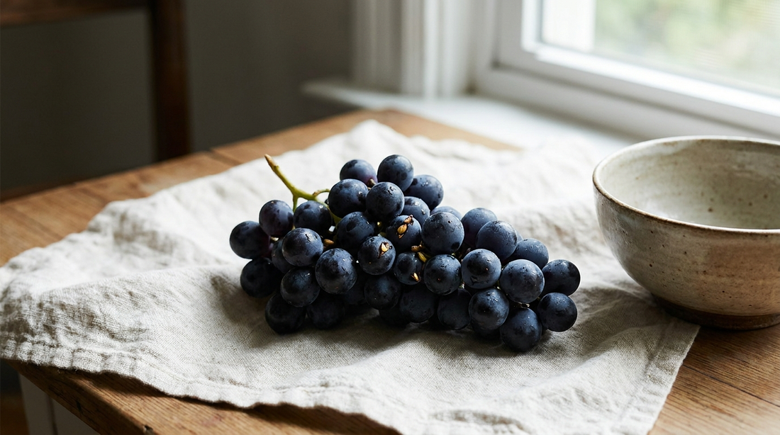 A cluster of dark purple grapes with seeds on cream linen.