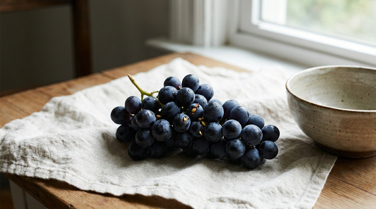 A cluster of dark purple grapes with seeds on cream linen.