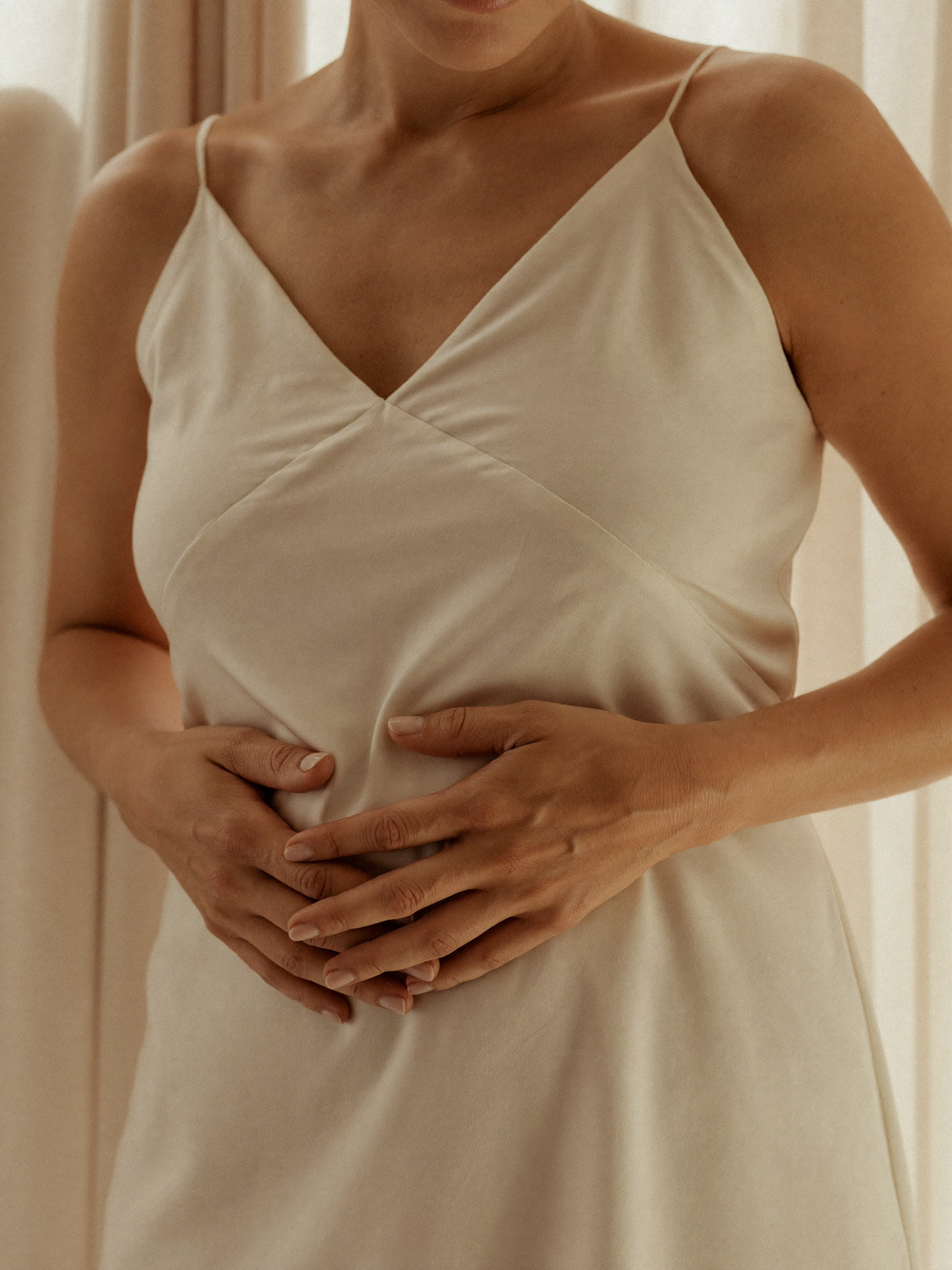 Woman in cream silk slip with both hands cradled gently at her midsection — Pre+Probiotic hero